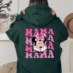 以下が含まれることがあります： ピンクと白のミニーマウスのグラフィックと「MAMA」という文字が4回繰り返された緑色のフード付きスウェットシャツです。