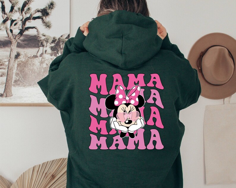 以下が含まれることがあります： ピンクと白のミニーマウスのグラフィックと「MAMA」という文字が4回繰り返された緑色のフード付きスウェットシャツです。