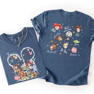 May include: Two blue t-shirts with Toy Story graphics. One shirt features a Mickey Mouse-shaped design with characters like Woody, Buzz Lightyear, and Jessie. The other shirt displays character faces and names like Slinky and Bo Peep.