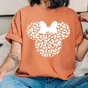 Peut inclure: Un t-shirt orange br&ucirc;l&eacute; avec une silhouette blanche d'une t&ecirc;te de Mickey Mouse &agrave; imprim&eacute; l&eacute;opard.