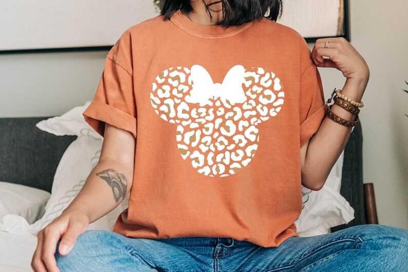 Peut inclure: Un t-shirt orange br&ucirc;l&eacute; avec une silhouette blanche d'une t&ecirc;te de Mickey Mouse &agrave; imprim&eacute; l&eacute;opard.