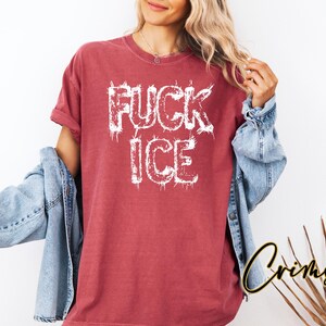 May include: A red t-shirt with the words "FUCK ICE" in white, distressed lettering. The model is wearing a denim jacket over the shirt. The shirt is a casual, oversized fit.