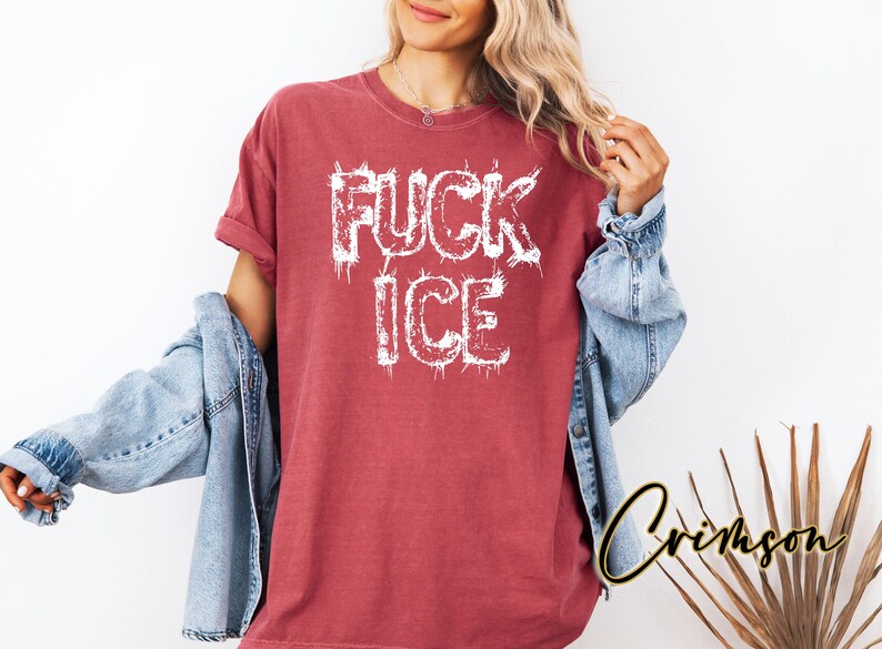 May include: A red t-shirt with the words "FUCK ICE" in white, distressed lettering. The model is wearing a denim jacket over the shirt. The shirt is a casual, oversized fit.