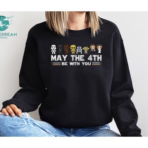 Op de afbeelding: Zwart sweatshirt met een afbeelding van Star Wars-personages en de tekst "Moge de 4e met je zijn".