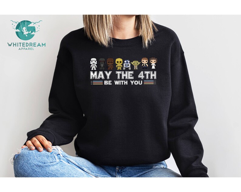 Op de afbeelding: Zwart sweatshirt met een afbeelding van Star Wars-personages en de tekst "Moge de 4e met je zijn".