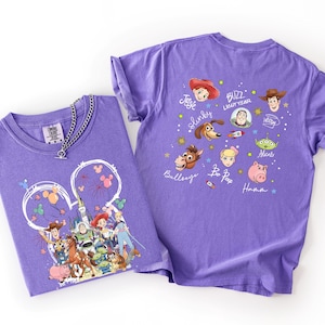 May include: Two purple t-shirts with Toy Story character graphics. One shirt features a Mickey Mouse head design with characters. The other shirt has character faces and names. A silver chain necklace is on one shirt.