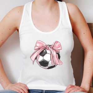 May include: White tank top with a pink bow and a black and white soccer ball graphic.
