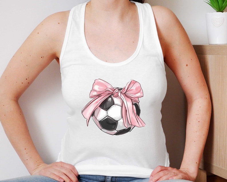 May include: White tank top with a pink bow and a black and white soccer ball graphic.