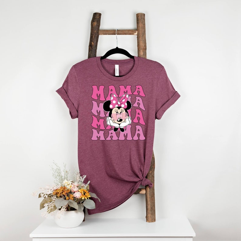 May include: A maroon t-shirt with a pink and white graphic of Minnie Mouse with the word "MAMA" repeated in a retro font.