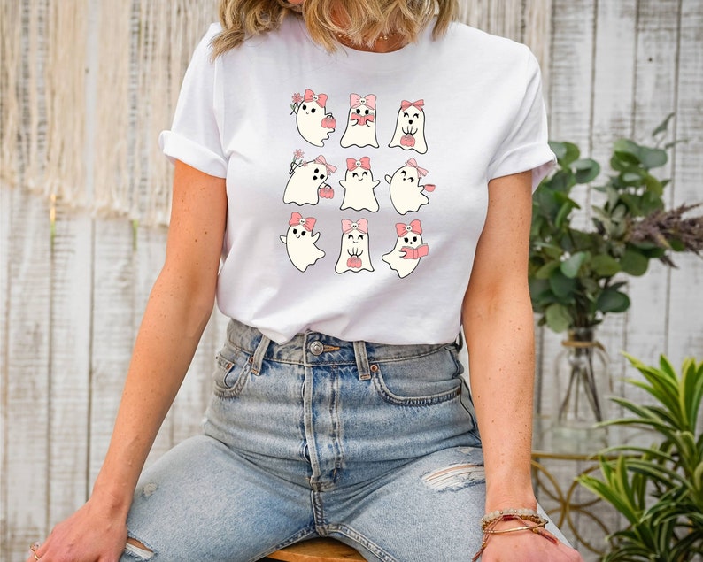 Puede incluir: Camiseta blanca con un gr&aacute;fico de nueve fantasmas lindos con lazos rosas y sosteniendo varios art&iacute;culos. Los fantasmas est&aacute;n dispuestos en un patr&oacute;n de cuadr&iacute;cula.