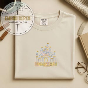 May include: Cream-colored sweatshirt with an embroidered Disney World castle design in yellow, blue, and pink. The text "Disney World" is embroidered below the castle. The sweatshirt has a Comfort Colors tag.