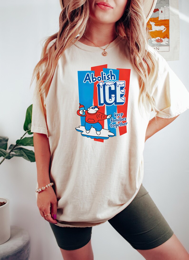 May include: Cream-colored t-shirt with a graphic that reads "Abolish ICE" in blue and red. The graphic features a cartoon polar bear holding a bottle. The text "keep families together" is also included.