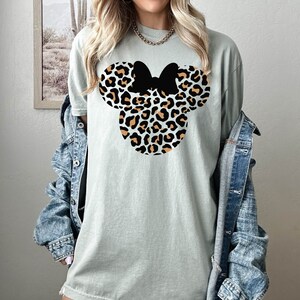 Peut inclure: Un t-shirt vert clair avec un motif de t&ecirc;te de Minnie Mouse imprim&eacute; l&eacute;opard. Le n&oelig;ud est noir.
