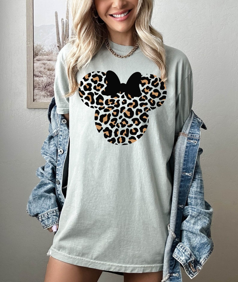 Peut inclure: Un t-shirt vert clair avec un motif de t&ecirc;te de Minnie Mouse imprim&eacute; l&eacute;opard. Le n&oelig;ud est noir.