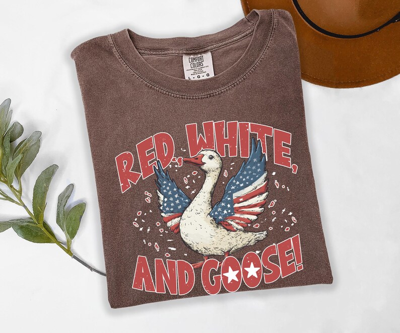 May include: Brown t-shirt with a distressed graphic of a goose with American flag-themed wings and the text "RED, WHITE, AND GOOSE!". The shirt has a crew neck and a Comfort Colors tag.