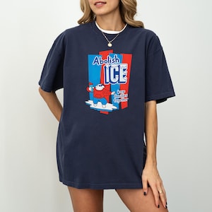 May include: Navy blue t-shirt with the words "Abolish ICE" and a cartoon character on a surfboard. The graphic is in red, white, and blue. The text "keep families together" is also included.