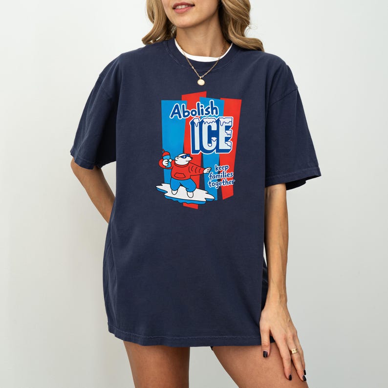 May include: Navy blue t-shirt with the words "Abolish ICE" and a cartoon character on a surfboard. The graphic is in red, white, and blue. The text "keep families together" is also included.