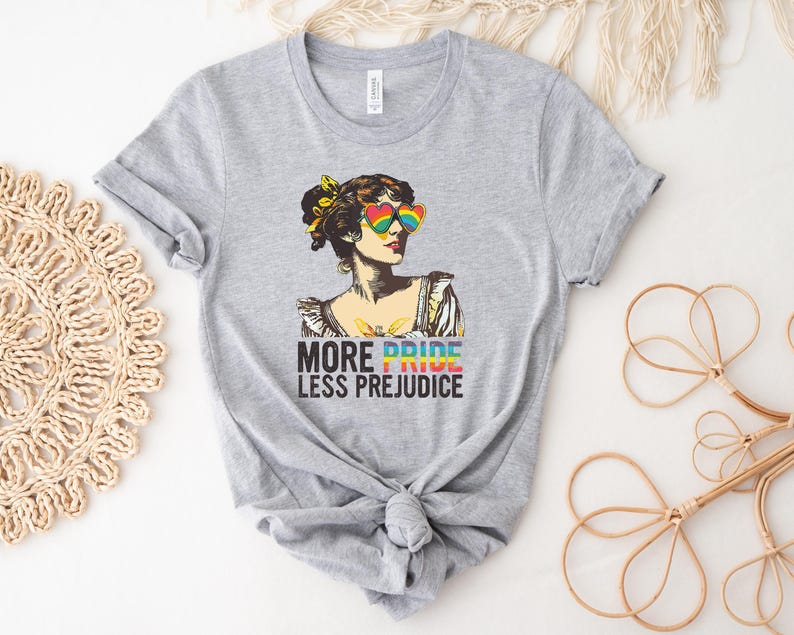May include: Gray t-shirt with a colorful illustration of a woman wearing rainbow heart-shaped sunglasses. The text "More Pride Less Prejudice" is printed below the illustration.