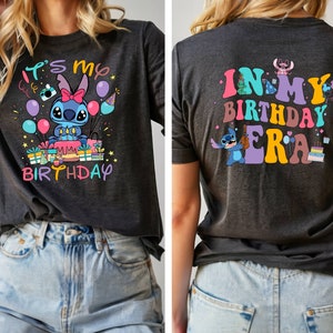 Puede incluir: Una camiseta gris oscuro con un personaje azul Stitch sosteniendo un pastel y globos. El texto en la parte delantera dice "It's my birthday". La parte posterior de la camiseta dice "In my birthday era" con un personaje azul Stitch tocando un ukelele.