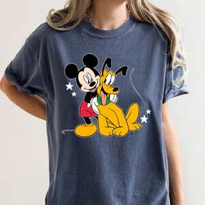 May include: A dark blue t-shirt with a cartoon image of Mickey Mouse and Pluto. Mickey Mouse is wearing red shorts and yellow shoes. Pluto is a yellow dog with a long tail. There are white stars in the background.