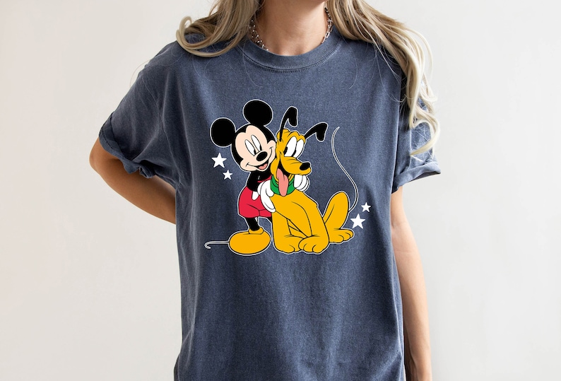 May include: A dark blue t-shirt with a cartoon image of Mickey Mouse and Pluto. Mickey Mouse is wearing red shorts and yellow shoes. Pluto is a yellow dog with a long tail. There are white stars in the background.