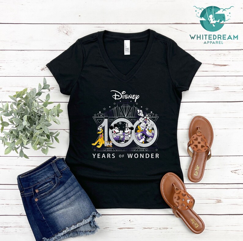 May include: Black V-neck t-shirt with a graphic of Mickey Mouse, Donald Duck, Goofy, and Pluto celebrating Disney's 100 Years of Wonder. The graphic is in silver and black with a diamond design.