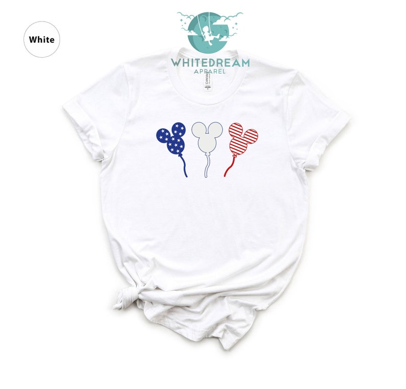 Puede incluir: Camiseta blanca con un gr&aacute;fico de tres globos con forma de Mickey Mouse. Los globos est&aacute;n decorados con rayas y estrellas rojas, blancas y azules, que recuerdan a la bandera espa&ntilde;ola.