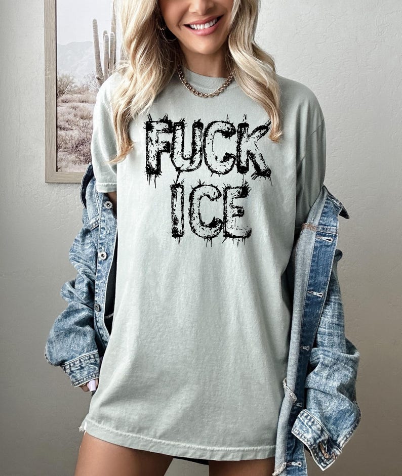 May include: A light green t-shirt with the words "FUCK ICE" printed in black, dripping font. The shirt is a relaxed fit and is being worn with a denim jacket.