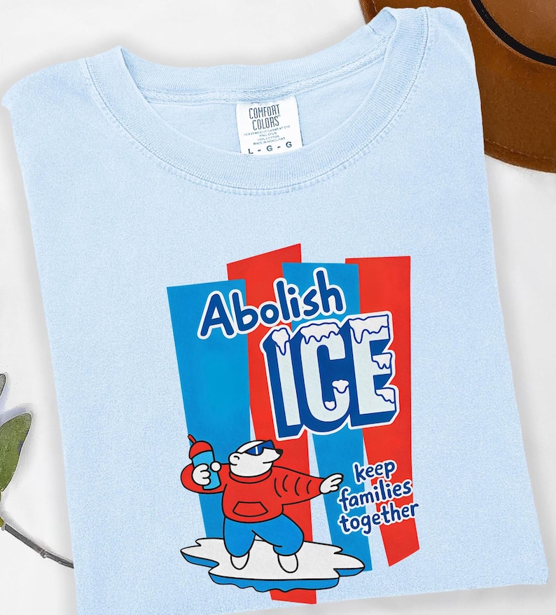 May include: Light blue Comfort Colors t-shirt with the words "Abolish ICE" in a graphic design. The design includes a polar bear holding a drink and the phrase "keep families together."