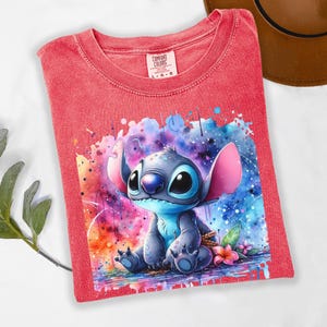 Pu&ograve; includere: T-shirt rosso Comfort Colors con un'illustrazione ad acquerello del personaggio Stitch. L'opera d'arte mostra Stitch in tonalit&agrave; di blu, con orecchie rosa e uno sfondo colorato. La maglietta &egrave; taglia L-G.