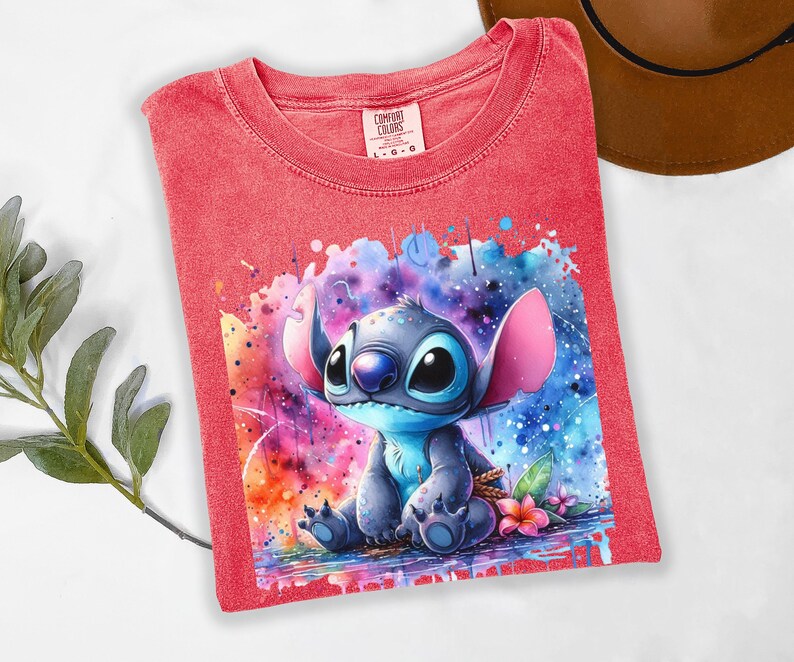 Pu&ograve; includere: T-shirt rosso Comfort Colors con un'illustrazione ad acquerello del personaggio Stitch. L'opera d'arte mostra Stitch in tonalit&agrave; di blu, con orecchie rosa e uno sfondo colorato. La maglietta &egrave; taglia L-G.