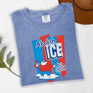 May include: A blue Comfort Colors t-shirt with a graphic that reads "Abolish ICE" in white and blue, with a cartoon polar bear holding a bottle. The text "keep families together" is also included.