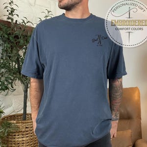 K&ouml;nnte beinhalten: Blaues T-Shirt mit kurzen &Auml;rmeln und dem aufgestickten Text "Best Dad" auf der Vorderseite. Das Shirt hat auch eine runde Grafik mit den Worten "Personalized Gift" und "Embroidered Comfort Colors".