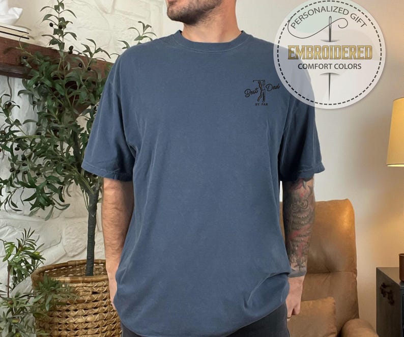 K&ouml;nnte beinhalten: Blaues T-Shirt mit kurzen &Auml;rmeln und dem aufgestickten Text "Best Dad" auf der Vorderseite. Das Shirt hat auch eine runde Grafik mit den Worten "Personalized Gift" und "Embroidered Comfort Colors".