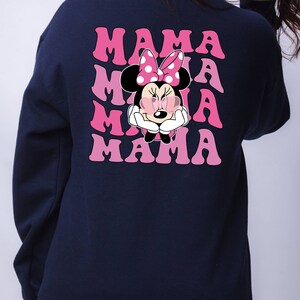 以下が含まれることがあります： ピンクのグラフィックでミニーマウスがサングラスとリボンをつけているネイビーブルーのスウェットシャツ。テキスト「MAMA」はピンクのグラデーションで4回繰り返されています。