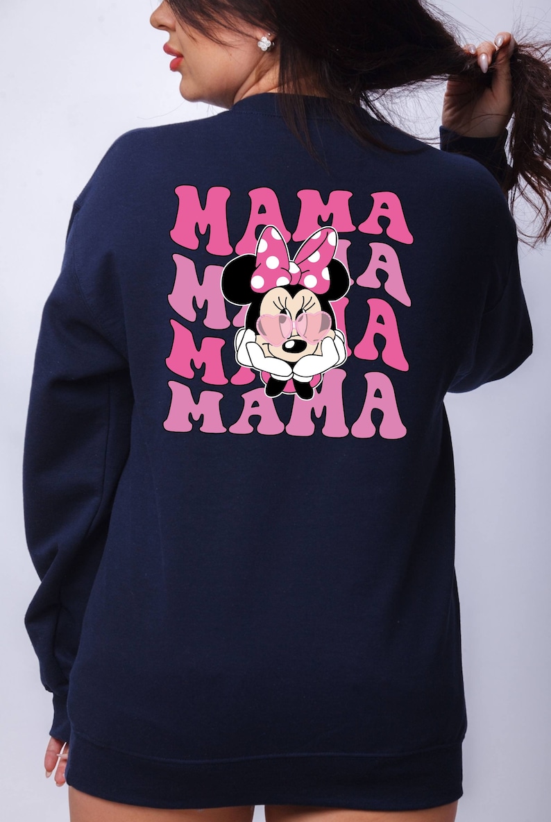 以下が含まれることがあります： ピンクのグラフィックでミニーマウスがサングラスとリボンをつけているネイビーブルーのスウェットシャツ。テキスト「MAMA」はピンクのグラデーションで4回繰り返されています。