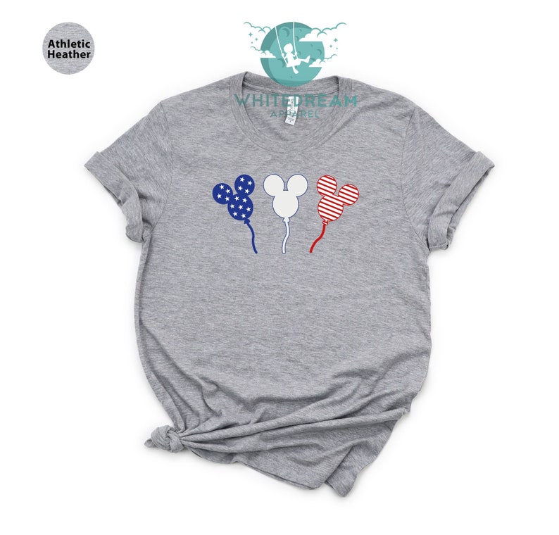 Puede incluir: Una camiseta gris con un dise&ntilde;o de tres globos con forma de cabeza de Mickey Mouse. Los globos est&aacute;n decorados con los colores de la bandera estadounidense: rojo, blanco y azul.