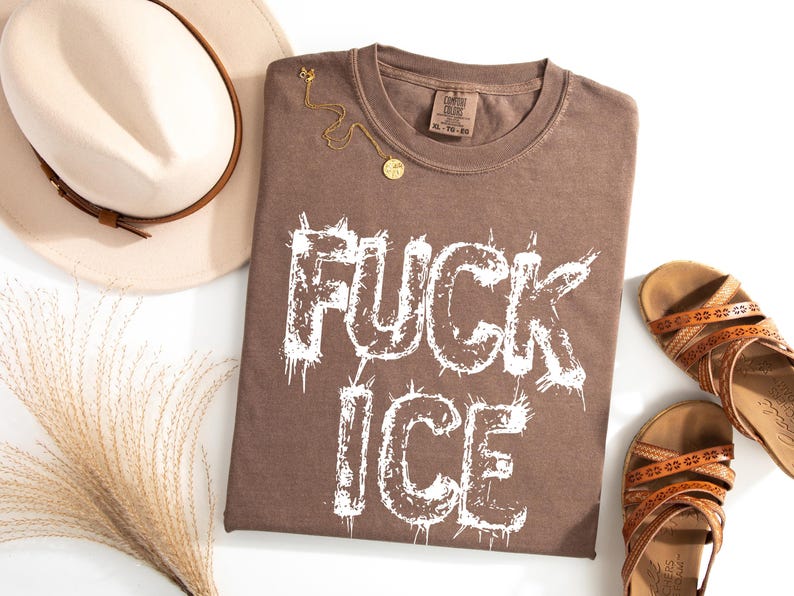 May include: A brown t-shirt with the words "FUCK ICE" in white, a gold necklace, a beige hat with a brown band, and brown sandals. The t-shirt has a crew neck and a tag that reads XL-TG-EG.