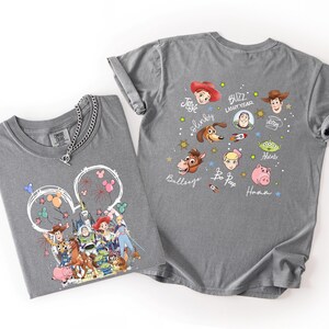 May include: Two gray t-shirts with Disney's Toy Story characters. One shirt features a Mickey Mouse head with fireworks and characters. The other shirt displays character faces and names like Buzz Lightyear and Woody.