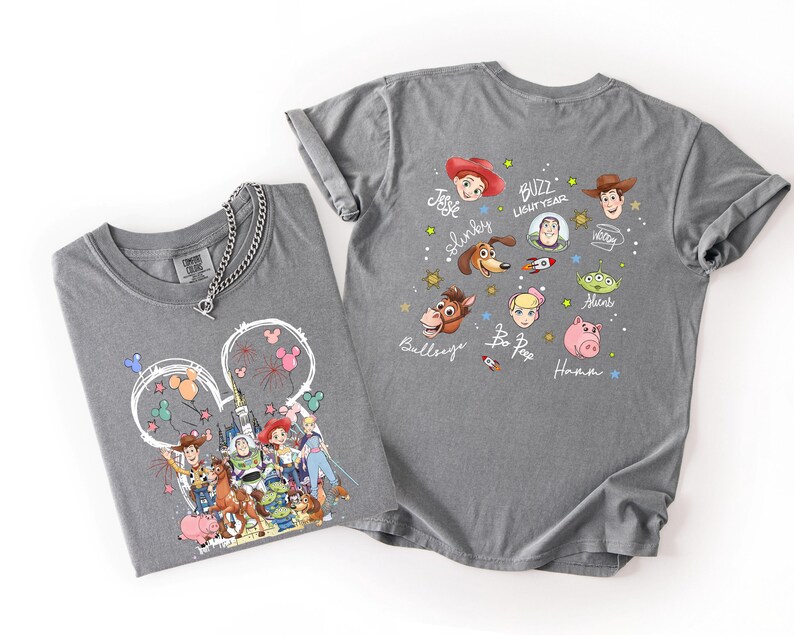 May include: Two gray t-shirts with Disney's Toy Story characters. One shirt features a Mickey Mouse head with fireworks and characters. The other shirt displays character faces and names like Buzz Lightyear and Woody.
