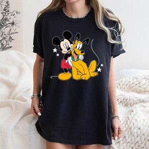 May include: Black t-shirt with a cartoon image of Mickey Mouse and Pluto. Mickey is wearing red shorts and Pluto is wearing a green collar.