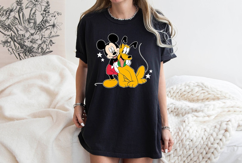 May include: Black t-shirt with a cartoon image of Mickey Mouse and Pluto. Mickey is wearing red shorts and Pluto is wearing a green collar.