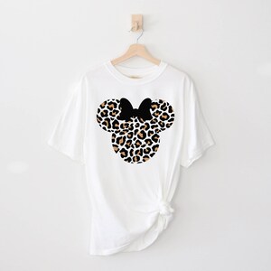 Peut inclure: T-shirt blanc avec un motif de t&ecirc;te de Minnie Mouse en imprim&eacute; l&eacute;opard noir et marron.