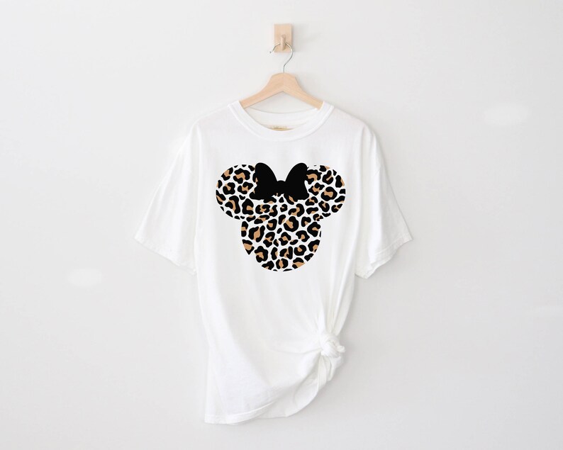 Peut inclure: T-shirt blanc avec un motif de t&ecirc;te de Minnie Mouse en imprim&eacute; l&eacute;opard noir et marron.