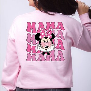 以下が含まれることがあります： ピンクのトレーナーに、サングラスとピンクのリボンをつけたミニーマウスのグラフィックがプリントされています。レトロなフォントで「MAMA」という文字が4回繰り返されています。