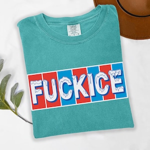 以下が含まれることがあります： ターコイズ色のTシャツ。白で「FUCKICE」の文字が青い縁取りで描かれ、赤と青のストライプの背景に配置されています。Tシャツは折りたたまれており、Comfort Colorsのタグが付いています。