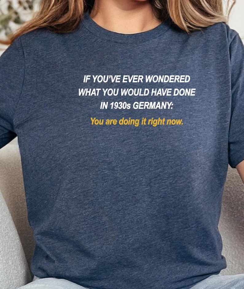 May include: A navy blue t-shirt with white text that reads "IF YOU'VE EVER WONDERED WHAT YOU WOULD HAVE DONE IN 1930s GERMANY: You are doing it right now."