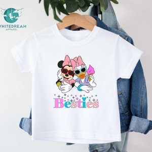 May include: White t-shirt with a graphic of Mickey Mouse and Daisy Duck wearing sunglasses and holding ice cream. The text "Bestiies" is printed below the graphic.