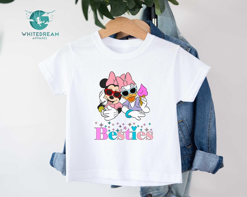 May include: White t-shirt with a graphic of Mickey Mouse and Daisy Duck wearing sunglasses and holding ice cream. The text "Bestiies" is printed below the graphic.