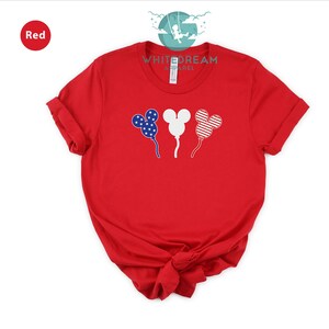 Puede incluir: Camiseta roja con un logotipo blanco "Whitedream Apparel" y tres globos con forma de Mickey Mouse con un dise&ntilde;o de bandera estadounidense.